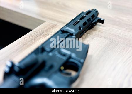 Schwarzes Gewehr im Stil AR-15 auf Holztisch in moderner Inneneinrichtung Stockfoto