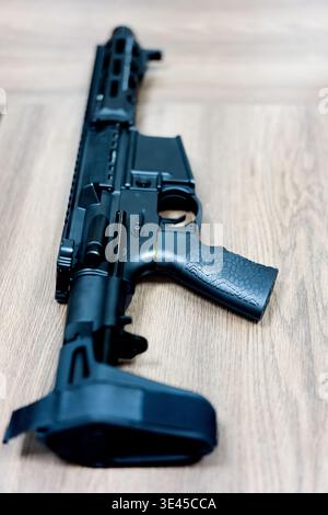 Schwarzes Gewehr im Stil AR-15 mit zusammenklappbarem Schaft auf Holzboden in Innenräumen Stockfoto