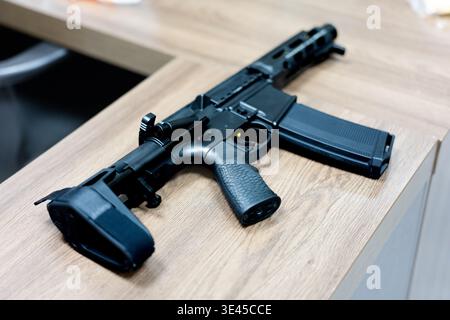 Schwarzes Gewehr im Stil AR-15 auf Holztisch in moderner Inneneinrichtung Stockfoto