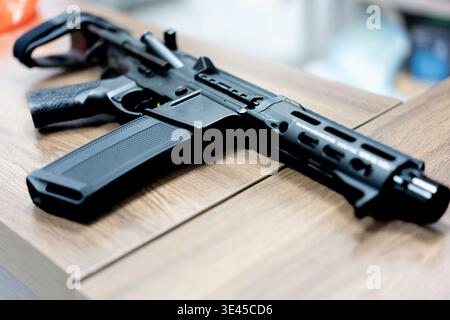 Schwarzes Gewehr im AR-15-Stil auf Holztisch im Innenbereich, modernes Schusswaffendesign Stockfoto