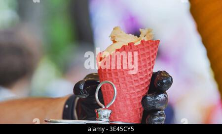 Hand hält ein erfrischendes Eis in einem leuchtenden roten Waffelkegel im Freien Stockfoto