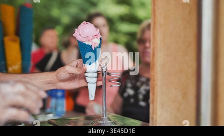 Servieren Sie Erdbeeren- und Vanilleeis in einem blauen Kegel am Verkaufsstand Stockfoto