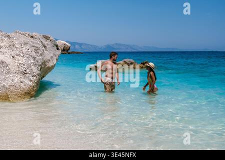 Im Herzen Sardiniens waten ein Paar durch das türkisfarbene Wasser, umgeben von atemberaubender Küstenlandschaft. Die Sonne scheint hell und untergeht Stockfoto