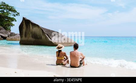 Ein abwechslungsreiches Paar sitzt friedlich am Sandstrand der Similan Islands, umgeben von klarem türkisfarbenem Wasser und atemberaubenden Felsformationen. Diese idyllische Umgebung ist perfekt für Romantik und Entspannung. Stockfoto