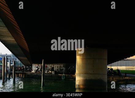 Venedig, Italien - 07. Februar 2026: Blick unter einer Brücke mit Betonsäule, Graffiti an der Wand und geparkten Motorrädern am Wasser Stockfoto