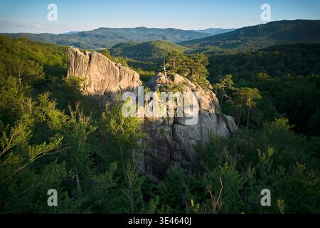 Blick aus der Vogelperspektive auf die Felsformation, die in warmes Sonnenlicht getaucht ist, zwischen üppig grünen Wäldern und sanften Hügeln. Dovbush Rocks, Karpaten, Ukraine. Stockfoto