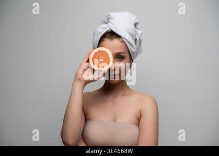 Frau, die sich auf eine natürliche Hautpflegeroutine vorbereitet, frische Grapefruit als natürliche Zutat für gesunde, strahlende Haut und Schönheitsbehandlungen zu Hause Stockfoto