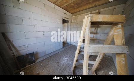 Neues Haus mit leerem Raum mit weißen Schlackenblockwänden und Holzleiter Stockfoto