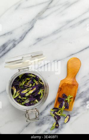 Löffel und trockene organische blaue Anchan auf Marmor Hintergrund Nahaufnahme. Kräutergesunder Tee. Schmetterlingserbsentee, trockene Blumen. Thailändische Küche. Selektiver Fokus, oben Stockfoto