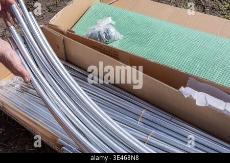 Gewächshaus-Kit zum Auspacken von Metallrohren und Abdeckmaterial in Pappkarton für die Vorbereitung der Garteninstallation Stockfoto