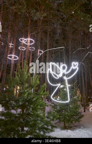 Leuchtende Neon-Engel-Lichtdekoration im Winter-Kiefernwald bei Nacht Stockfoto