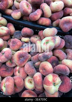 Flache Pfirsiche in einem Korb auf einem Markt mit frischen Produkten und leuchtenden Farben. Mobiles Foto Stockfoto