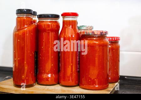 Glasflaschen und Gläser gefüllt mit hausgemachter roter Tomatensoße oder Ketchup auf einem Brett. Lebensmittelkonservierung, Winterlagerung, Bio-Produkte. Stockfoto