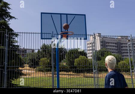 Junger Mann, der vor einem blauen Basketballkorb steht, mit einem Ball, der durch das Netz läuft Stockfoto