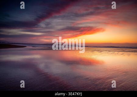 Dramatischer Sonnenuntergang Über Ruhigem Strand Mit Farbenfrohem Himmel Und Spiegelähnlichem Nassem Sand, Valdovino, Spanien Stockfoto