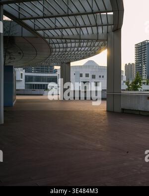 Leerer gepflasterter städtischer platz mit einem modernen Lattendach, der während des Sonnenuntergangs starke geometrische Schatten wirft. Die Szene repräsentiert die Zeitgenossen Stockfoto