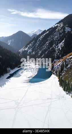 Aus der Vogelperspektive auf den gefrorenen Kolsay-See, umgeben von dichten Kiefernwäldern und schneebedeckten Berggipfeln in Kasachstan. Stockfoto