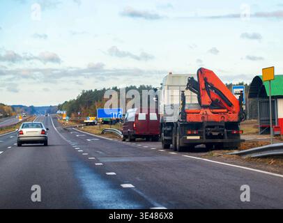 Weitläufige Sicht auf den Straßenverkehr mit fahrenden und angehaltenen Fahrzeugen. Silver Limousine fährt von der Kamera weg. Roter Service-Van und schwerer Lkw mit Stockfoto
