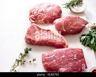 Rohe Stücke von Rib-Eye, Roastbeef, Flank Steak und Rumpsteak werden auf einem Schneidebrett angeordnet. Frische Kräuter und Salz stehen in der Nähe in einer Küche. Zutat Stockfoto