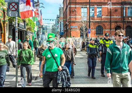 Mann mit grünem Shamrock-T-Shirt und Hut, Menschenmassen und Garda-Polizei, Gardai auf einer belebten Straße während des St. Patrick’s Day Festivals in Dublin Stockfoto