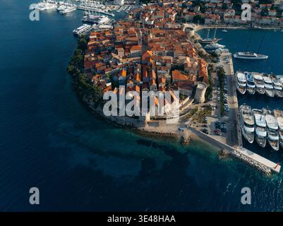 Blick aus der Vogelperspektive auf die Terrakotta-Dächer, die hinunterstürzen und auf das azurblaue Wasser treffen, das die alten Steinmauern der historischen Stadt Korčula, Dubrovni umgibt Stockfoto