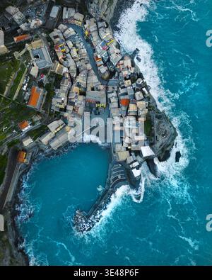 Aus der Vogelperspektive auf das farbenfrohe Küstendorf mit seinem kleinen Hafen und den stürzenden türkisfarbenen Wellen gegen den Steinpier Vernazza, Ligurien, Italien. Stockfoto