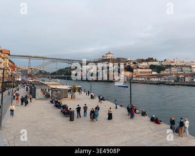 Blick auf die Menschen, die entlang der Uferpromenade schlendern, während der Fluss Douro unter der Brücke Dom Luís i fließt, Porto, Bezirk Porto, Portugal. Stockfoto