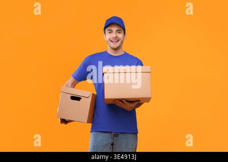 Der Lieferer hält während des Bright Day zwei Kartons vor orangem Hintergrund Stockfoto