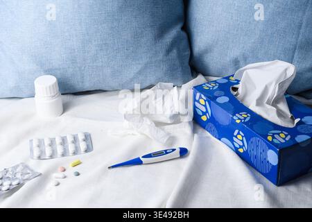 Häusliche Pflegeszene mit Taschentüchern, Thermometer, Pillen und Medikamentenflasche auf Bettwäsche, Krankheit und Genesungskonzept. Stockfoto