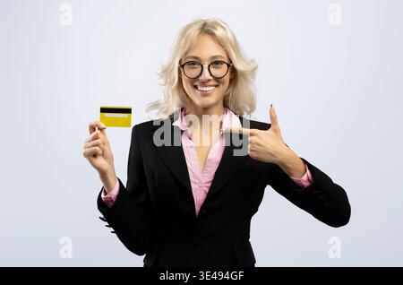Eine Frau, die einen Anzug trägt, hält eine gelbe Karte und lächelt die Kamera an, während sie darauf zeigt Stockfoto
