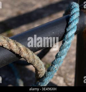 Nahaufnahme eines dicken, verwitterten Seils, das um eine dunkle Metallstange gebunden ist. Stockfoto
