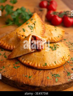 Authentische Empanadas aus argentinischem Rindfleisch, handgemacht mit Tomaten auf einem Holzbrett Stockfoto