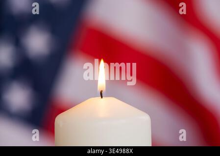 Beleuchtete Kerze mit Flamme vor verschwommenem Hintergrund der USA-Flagge, Symbol für Erinnerung, Patriotismus und Einheit. Stockfoto