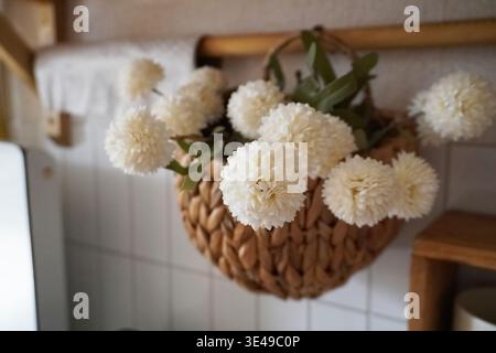 Schöne Anordnung von weißen Blumen in einem gewebten Korb, der auf einem Holzgestell hängt Stockfoto