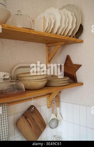 Eine gemütliche Küche mit Tellern, Schüsseln und Holzutensilien auf rustikalen Regalen für häusliche Ästhetik Stockfoto