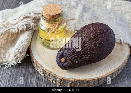 Reife braune Avocado, Kernel Öl Glasflasche auf Holztablett. Pflanzliches Bio-Öl zum Kochen von Lebensmitteln oder zur Hautpflege. Stockfoto