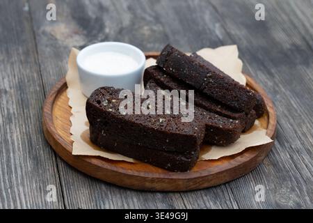 Schwarzer Knoblauchbrot mit weißer Sauce auf einem Holzbrett. Stockfoto