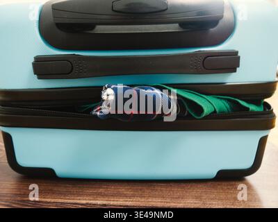 Blauer Koffer mit teilweise sichtbarer Kleidung auf einer Holzoberfläche Stockfoto