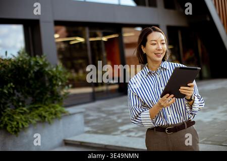 Eine Koreanerin steht vor einem modernen Gebäude. Sie hält eine Tafel in der Hand und scheint sich auf das zu konzentrieren, was sie tut. Die Umgebung ist hell, und sie Stockfoto