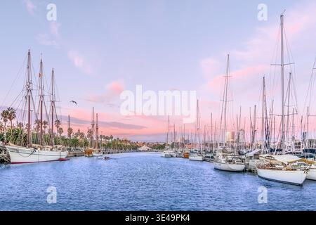 Yachten und Piratenschiffe liegen bei Sonnenuntergang im Hafen von Barcelona, Spanien. Meereslandschaft mit rosa-violettem Himmel und Palmen am Ufer Stockfoto