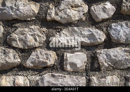 Nahaufnahme einer zerklüfteten Steinmauer mit unebenen Felsen und rauen Mörtelfugen bei hellem Licht Stockfoto
