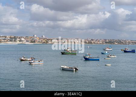 Blick auf die Küste von Cascais mit mehreren Booten auf dem ruhigen blauen Ozean und die Stadt in der Ferne unter klarem Himmel. Stockfoto