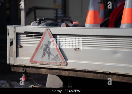 Die Heckklappe des sonnendurchfluteten städtischen Arbeitswagens mit einem verwitterten dreieckigen Schild für Baustellen, orangefarbenen Kegeln und gewickelten Kabeln; abgenutzte Metallverkleidungen, Schmutz A Stockfoto
