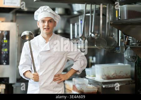 Junge männliche Köchin in Uniform stehend mit Schaufel in der Hand Stockfoto