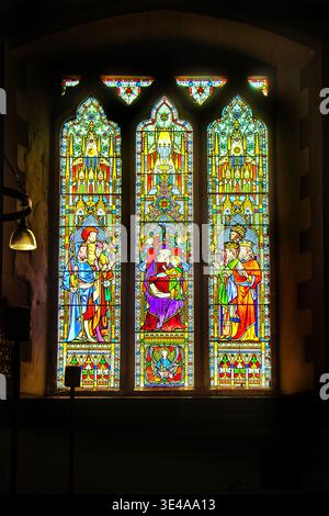 Ein gotisches Buntglasfenster, das die Anbetung der Magier mit der Jungfrau maria und dem Kind in einem Steinkircheninnenraum darstellt Stockfoto