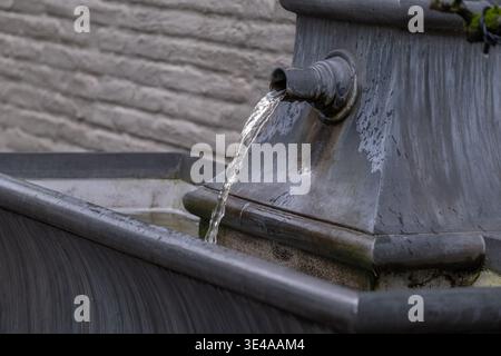 Fließendes Wasser aus Metallbrunnen in urbaner Umgebung mit weichem Licht und Texturdetails. Sauberer Wasserstrahl und minimale Zusammensetzung geeignet f Stockfoto