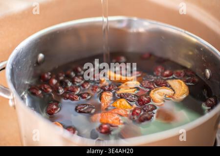 Obstpunsch machen. Nahaufnahme eines Topfes mit Wasser, in dem getrocknete Hagebutten, Äpfel und Orangenschalen schwimmen, was den Prozess von mA demonstriert Stockfoto