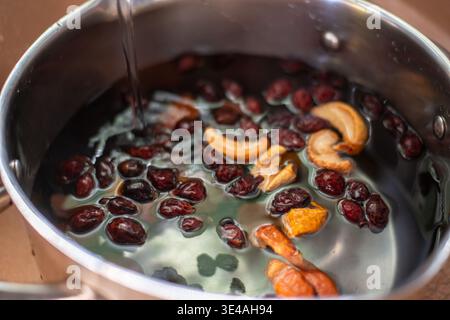 Obstpunsch machen. Nahaufnahme eines Topfes mit Wasser, in dem getrocknete Hagebutten, Äpfel und Orangenschalen schwimmen, was den Prozess von mA demonstriert Stockfoto