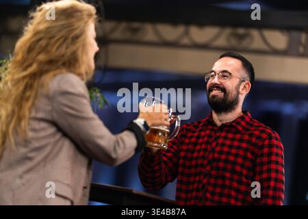 Freunde, die bei einer fröhlichen Feier in einem lebhaften Pub mit Bierkrügen anstoßen und in einem geselligen Treffen mit guter Stimmung miteinander und Glück genießen Stockfoto