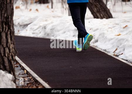 Ein Läufer in heller Sportausrüstung joggt auf einem freigelegten Weg, umgeben von Winterschnee Stockfoto